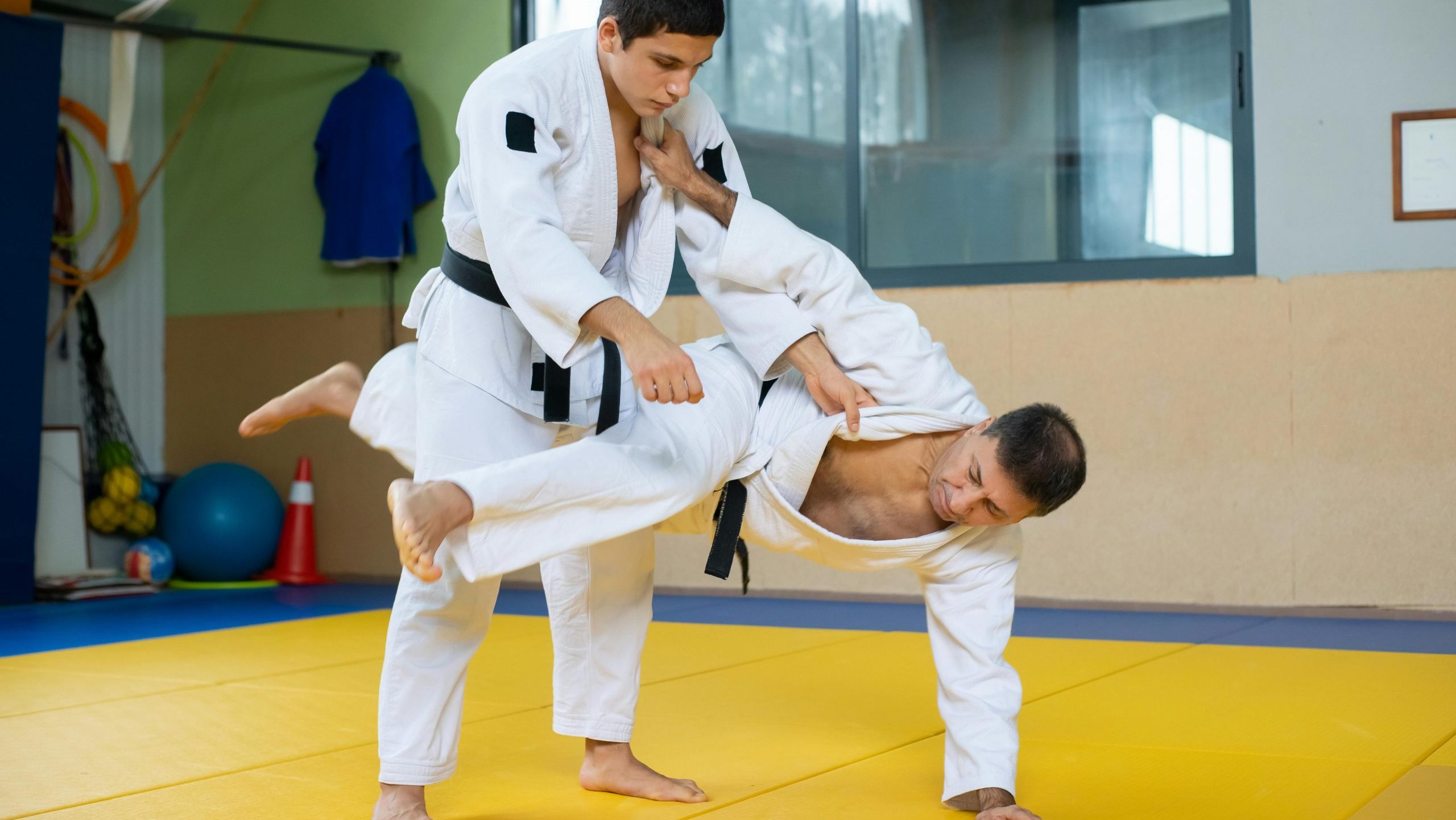 Dynamic action shot of two men practicing judo, showcasing technique and movement in an indoor gym setting.