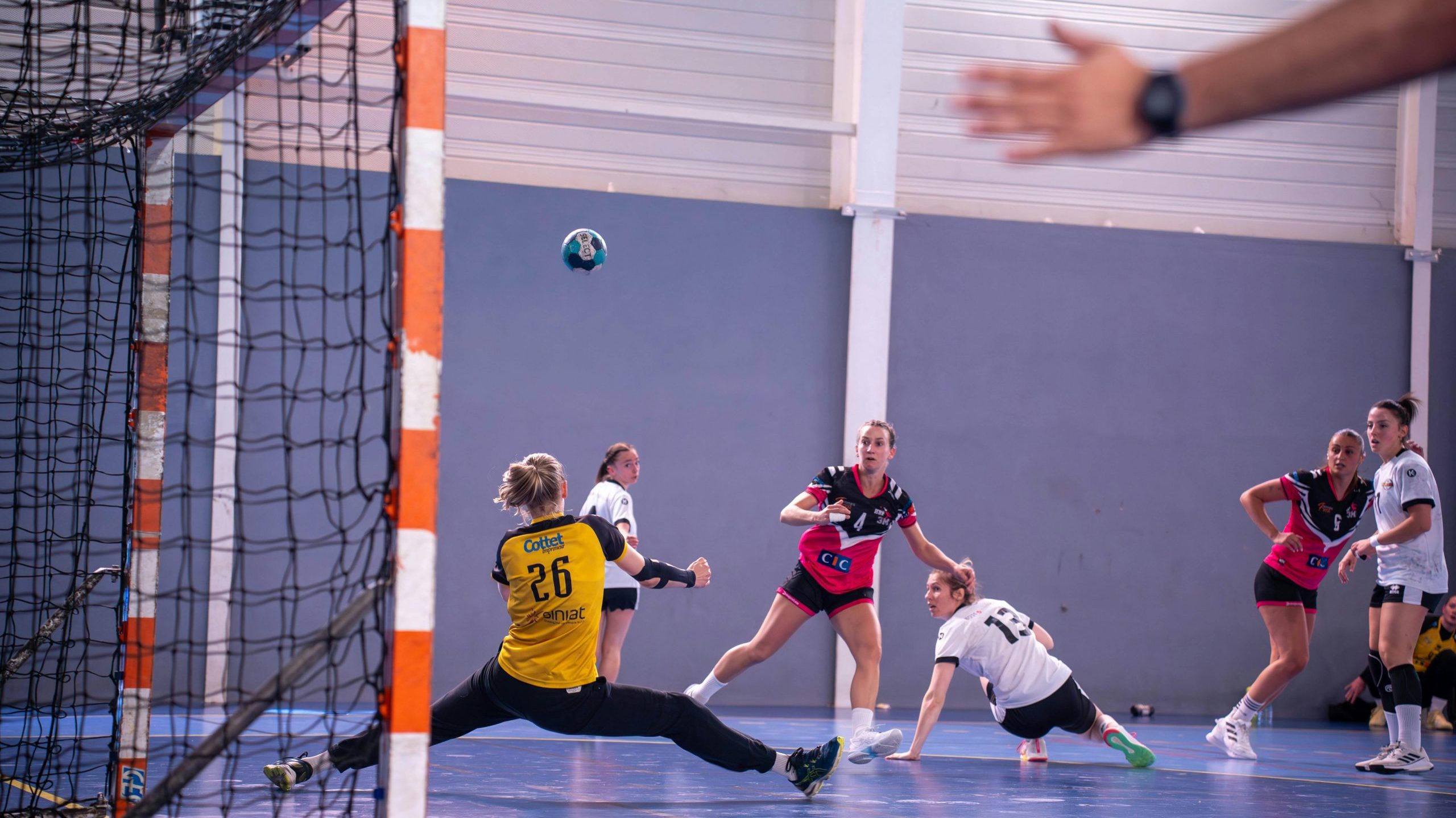 Dynamic action shot of a women's handball match with players in mid-movement.